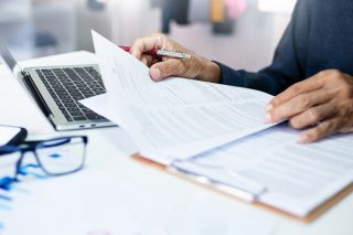 Foto: Person mit Dokumenten und Laptop